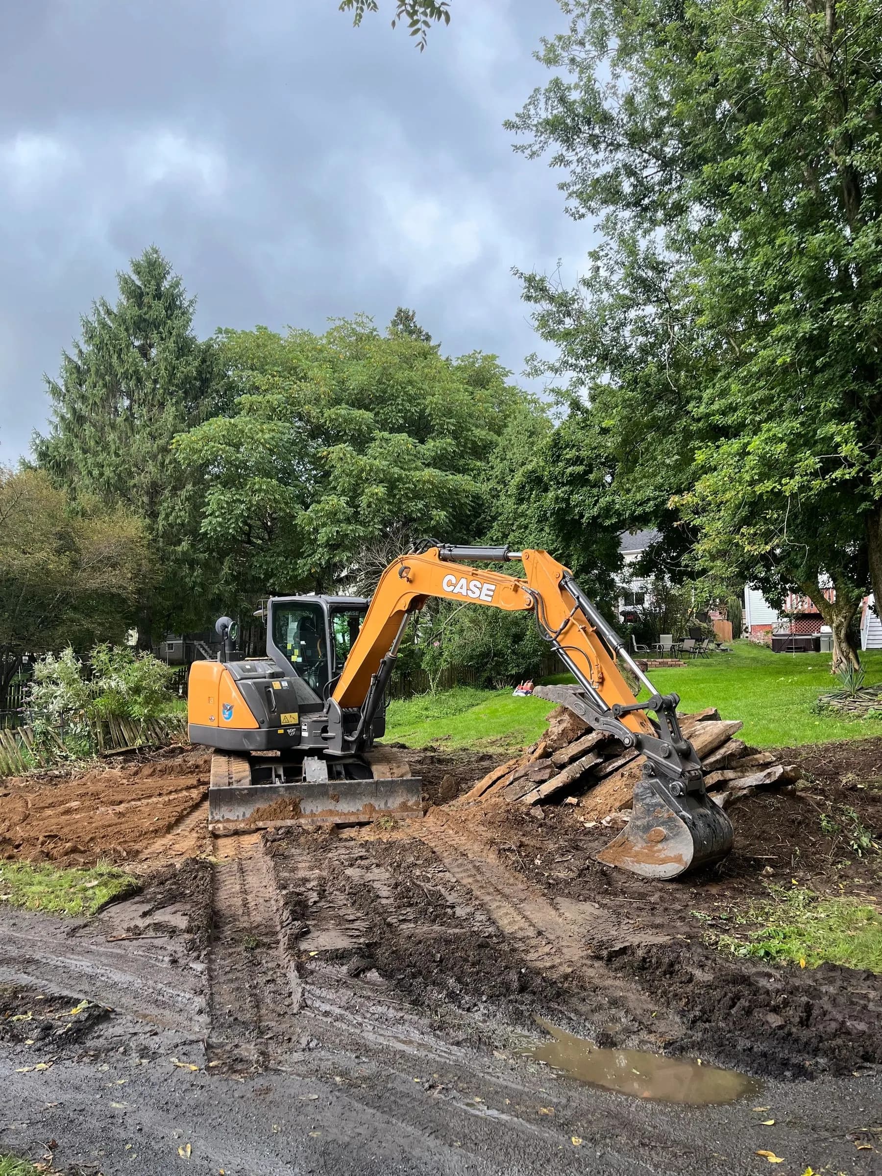 A CASE excavator on a torn-up residential site with soil pushed aside and houses in the background.