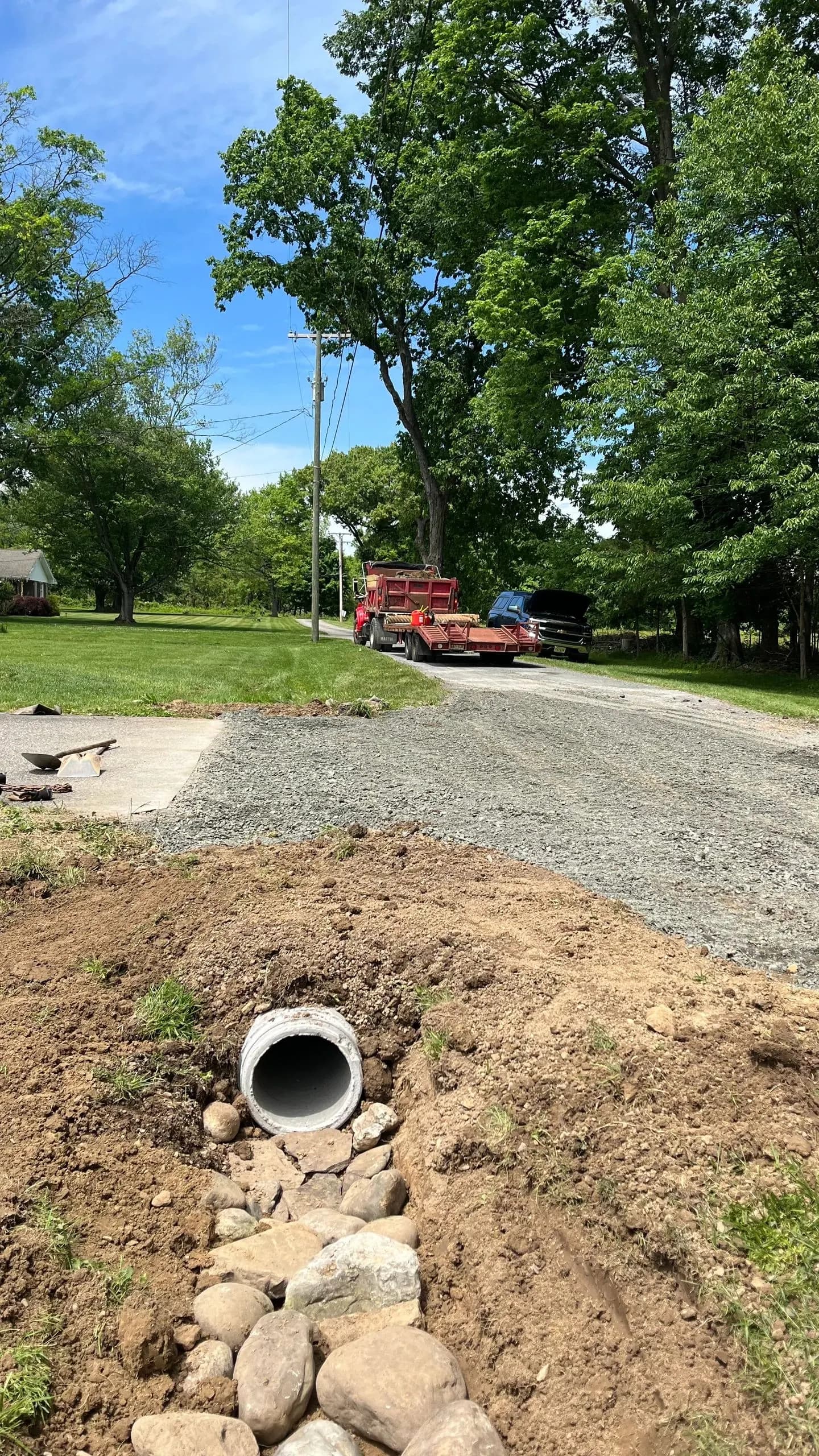Gravel driveway under construction with a culvert pipe set in the soil at the near end.