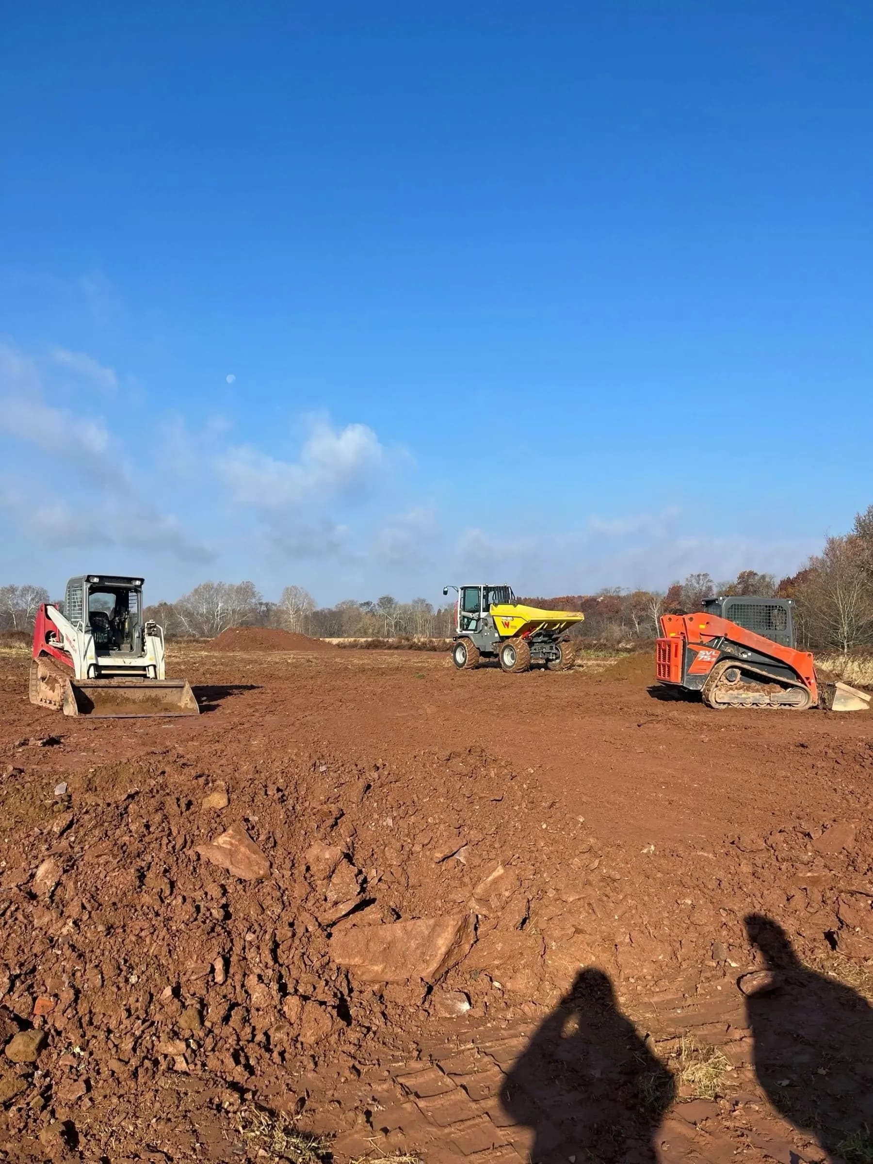 Three machines staged on a wide cleared site before grading.
