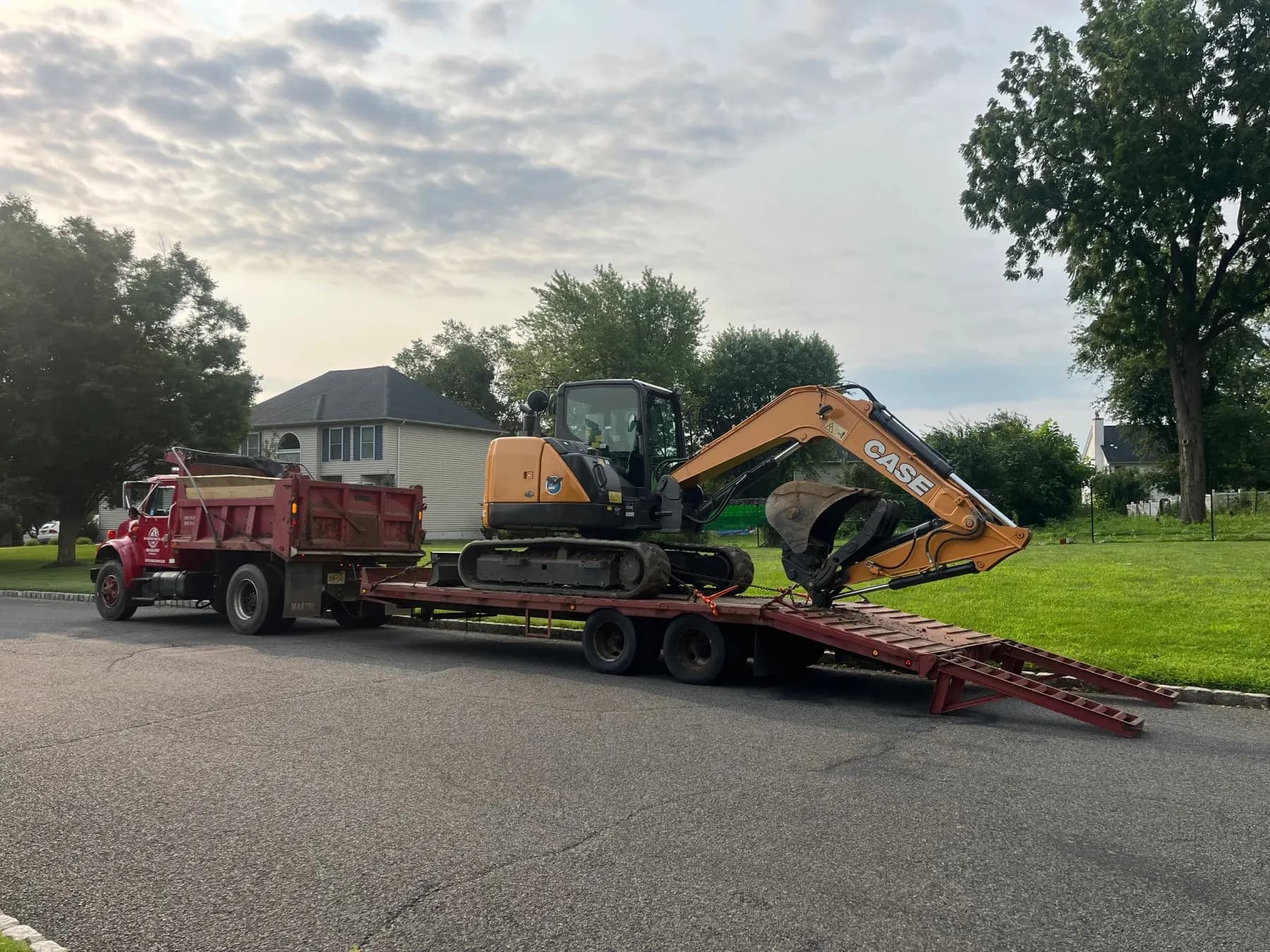 TM Contracting dump truck hauling a CASE excavator on a trailer through a residential street.